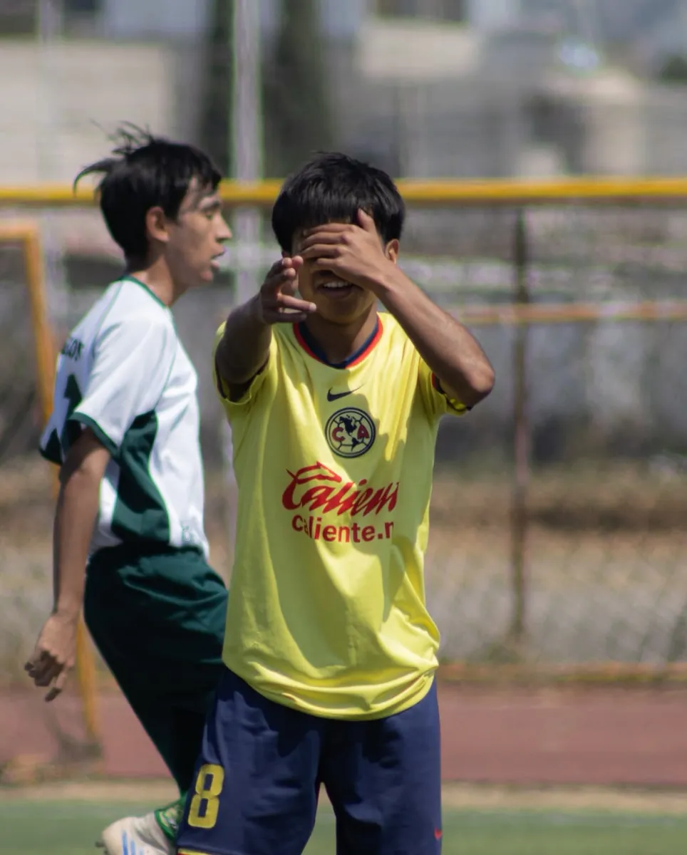 Jugador de Nido Águila con camiseta amarilla cubriéndose el rostro durante un partido junto a un rival