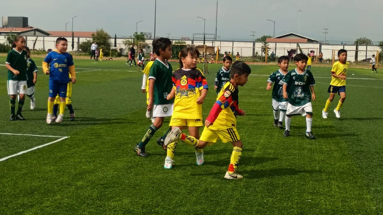 Niñas y niños de Nido Águila Valle de Chalco jugando un partido de fútbol en cancha de pasto sintético