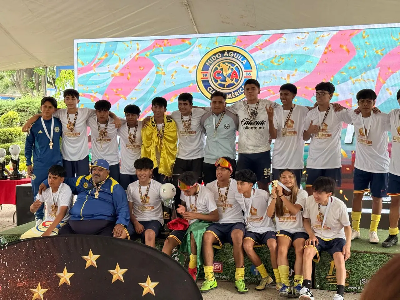 Equipo campeón de Nido Águila en el podio con medallas y trofeo frente a la pantalla con el escudo del Nido